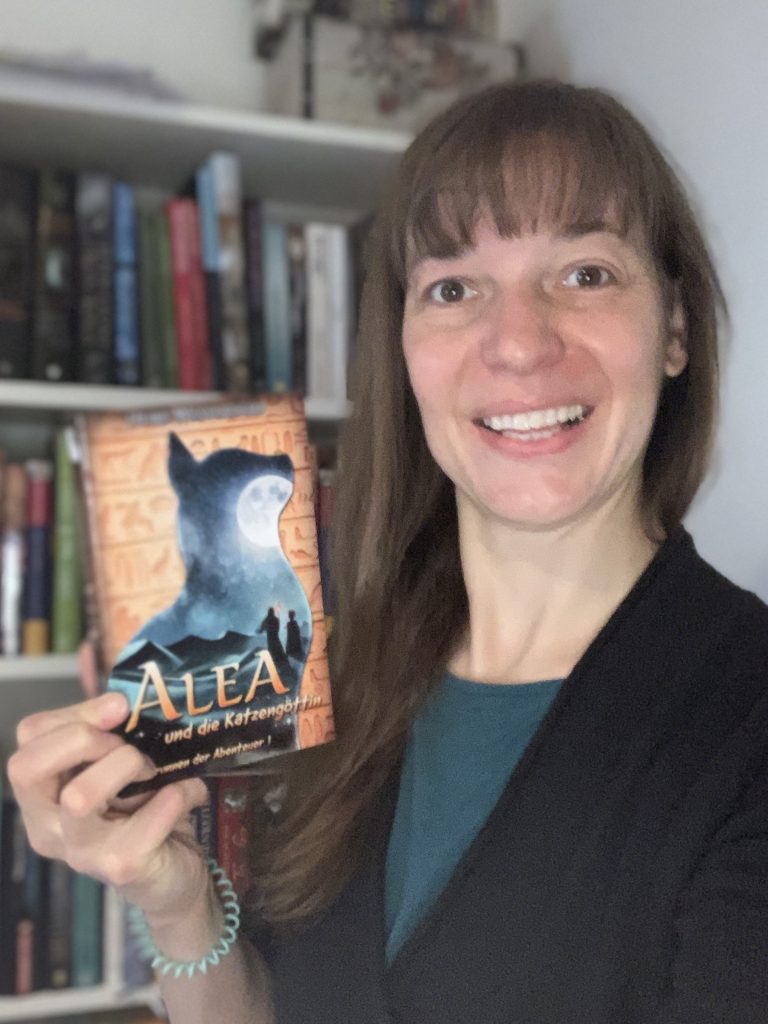 Autorin Heike Westendorf zeigt ihr Buch Alea und die Katzengöttin vor einem Bücherregal